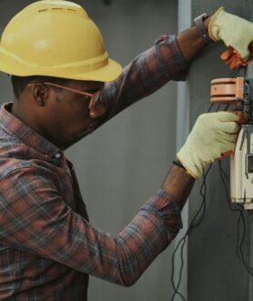 man in brown and white plaid dress shirt and yellow hard hat holding black and orange